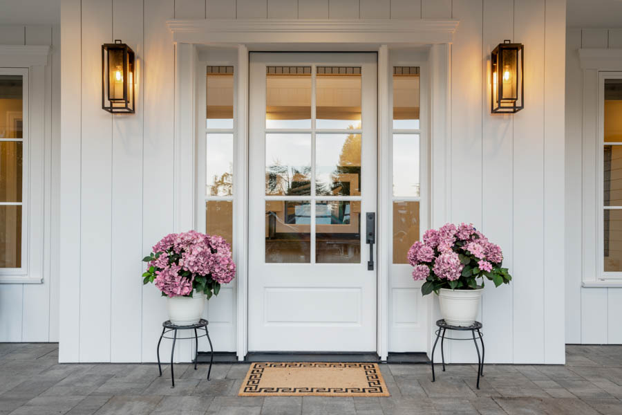 White front door flanked by two pots of pink flowers.