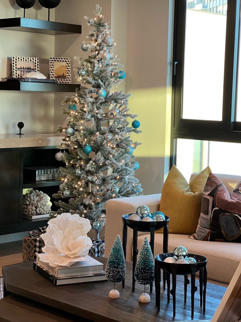 A Christmas tree decorated with silver and blue ornaments, set against a contemporary living room backdrop.