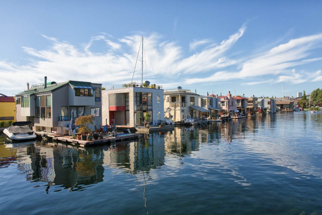 Floating homes atop smooth water, with blue skies and streaks of cloud above
