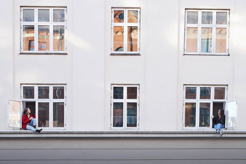 Young female neighbors talking from apartment windows