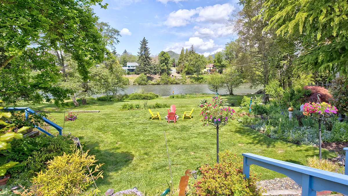 Image of a lush backyard leading out to a river, with red and yellow Adirondack chairs.