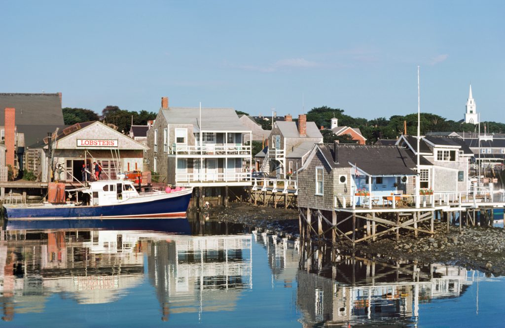 a boat in the water, and homes and a lobster shack on stilts, atop a beach at low tide
