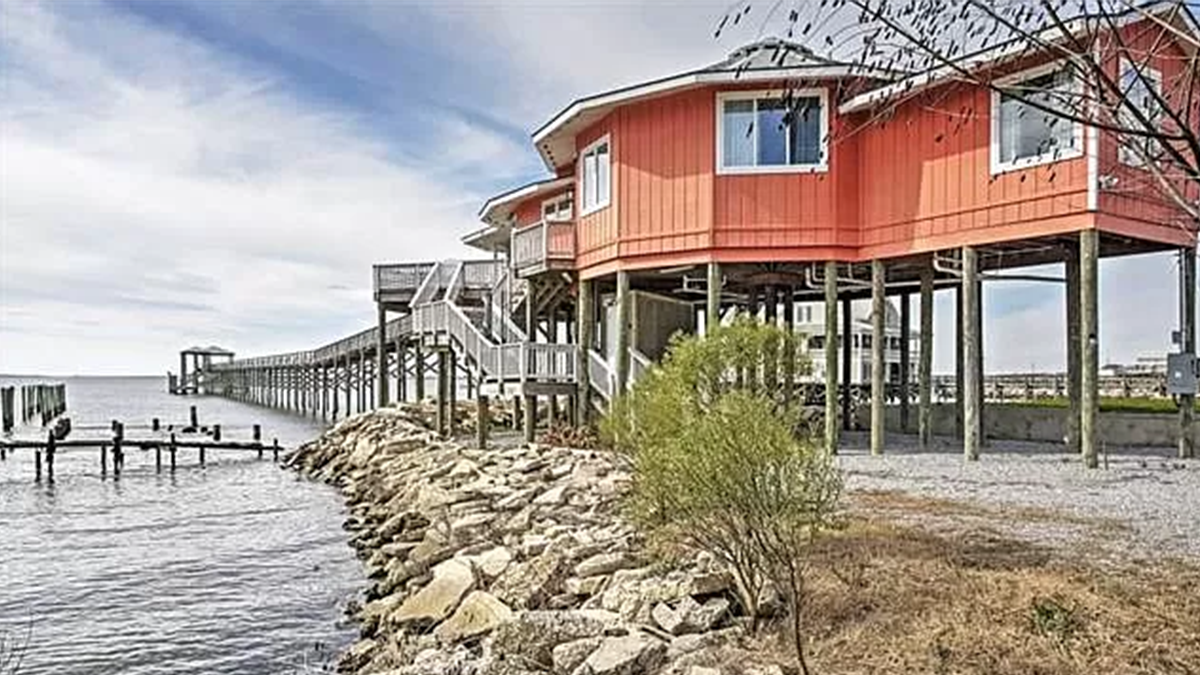 Image of a red house on stilts overlooking the water.