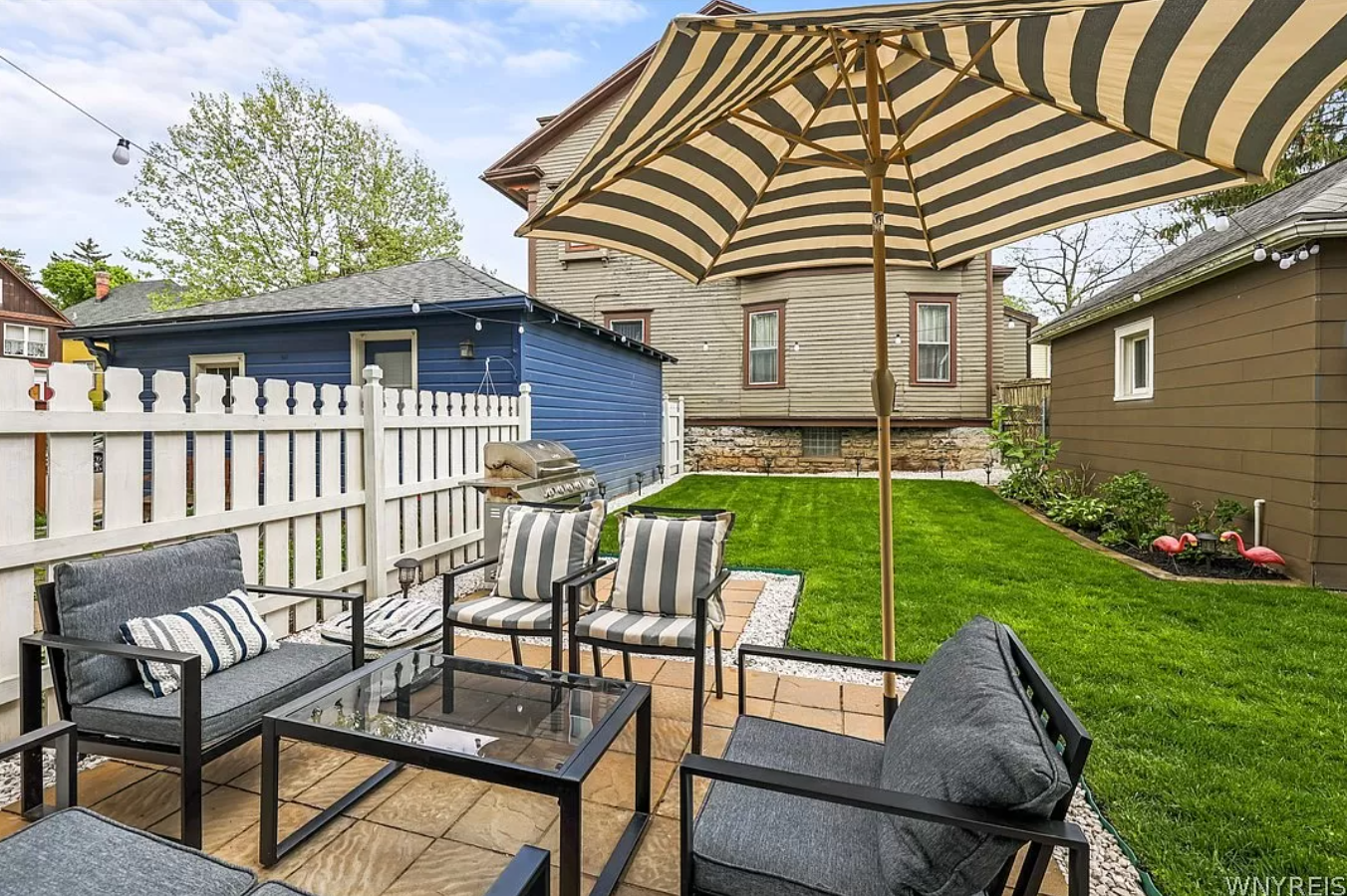 Image of a backyard with four chairs, a coffee table, and a striped umbrella.