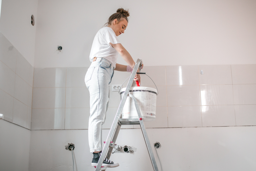 A woman on a ladder painting a wall.