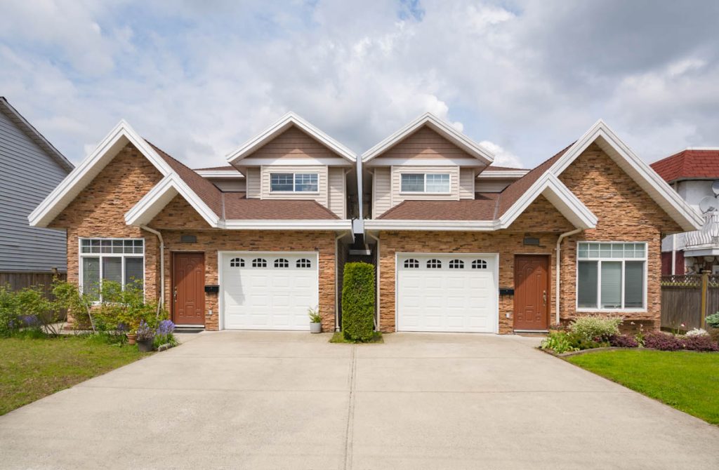 Residential duplex house with concrete driveway and green lawns in front