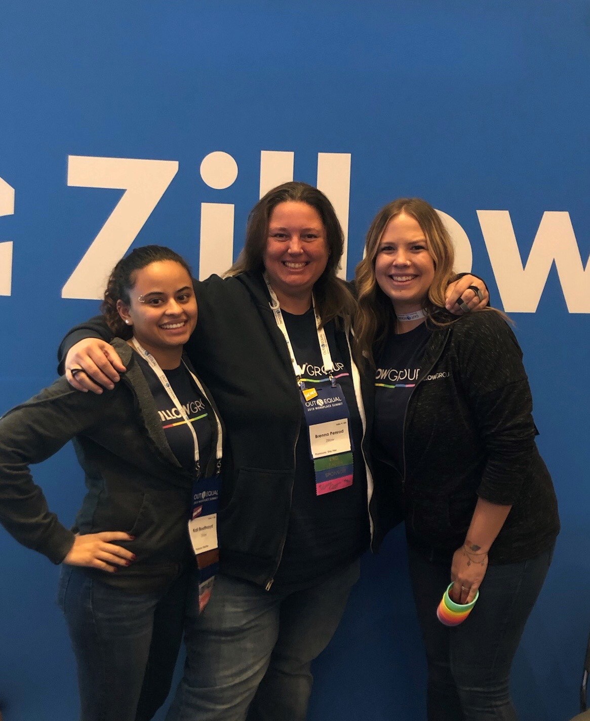 Three Zillow Pride affinity network members posing shoulder to shoulder with Zillow brand banner behind them.