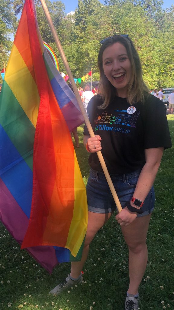 Zillow employee Katie Kull holding pole of large pride flag. She is waving the flag. 