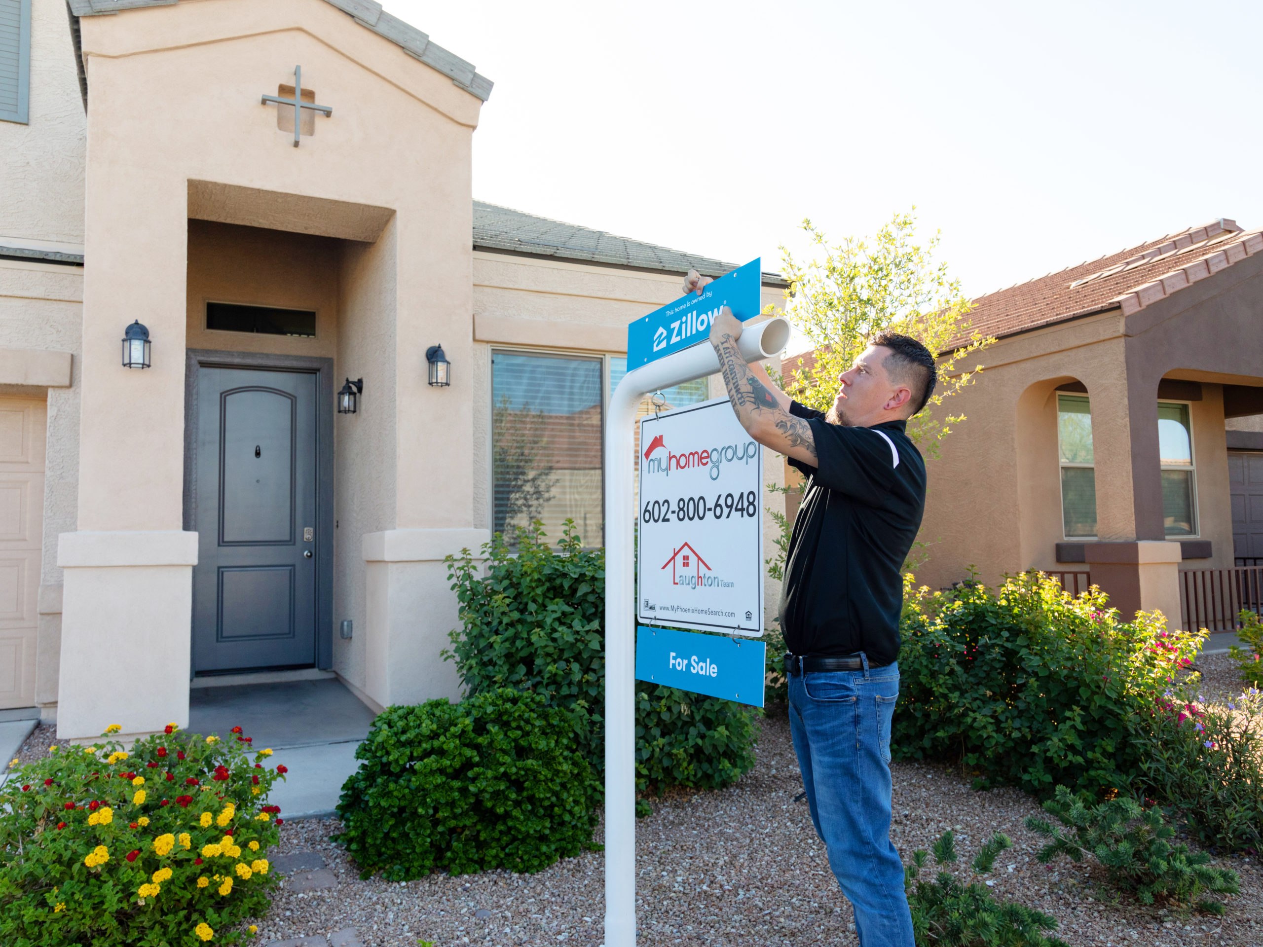Worker installing Zillow Offers for sale sign in front of single family home