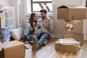 Man and woman sitting on floor surrounded by boxes with mugs after moving to NYC