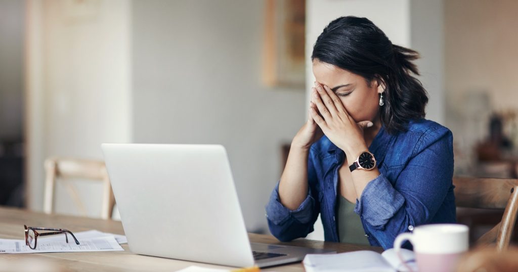 Shot of a young woman looking stressed while using a laptop at home